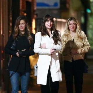 Dakota Johnson in a white coat walks with her friends