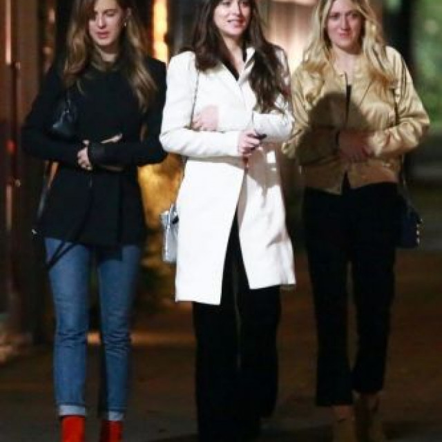 Dakota Johnson in a white coat walks with her friends